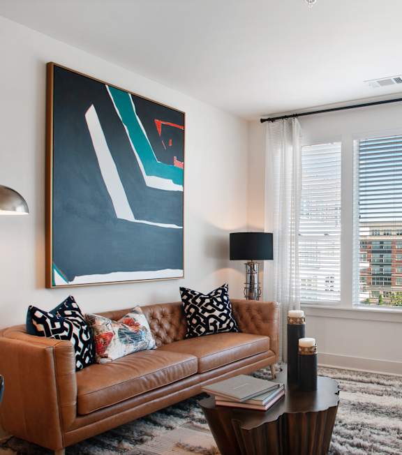 A living room with a brown couch and a large painting on the wall.