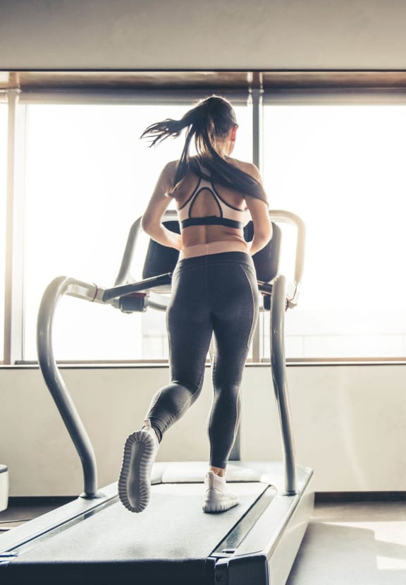 Man and woman running on treadmills in a gym with large windows.