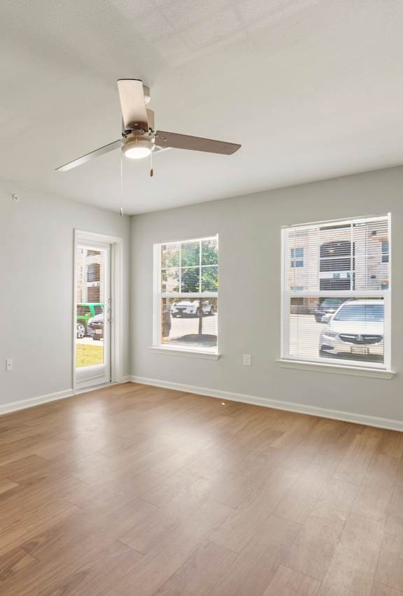 A room with a white door, a ceiling fan, and a window showing a parking lot outside.