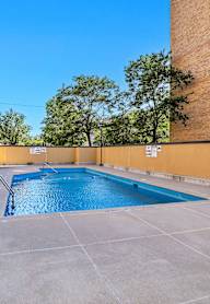A small pool surrounded by a concrete floor and a building.