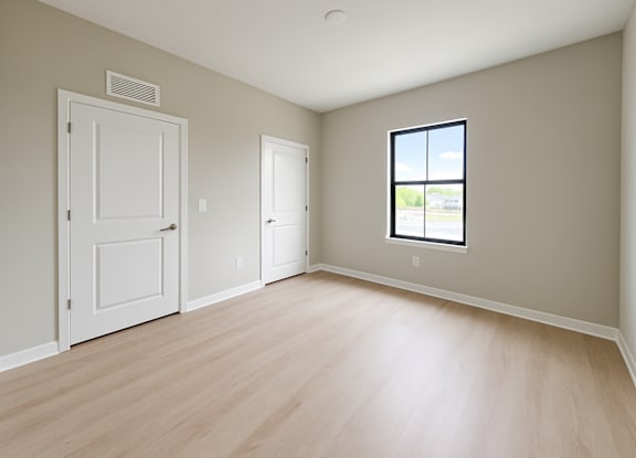 A room with a white door, a window, and a wooden floor.