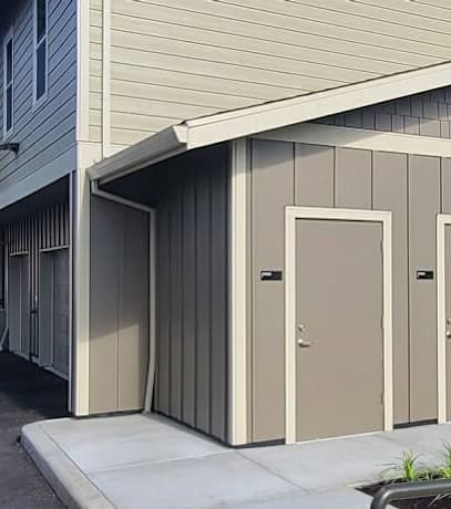 A small building with four doors is situated in front of a house.