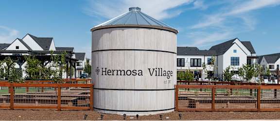 A large silo with the words Hermosa Village on it in front of a row of houses.