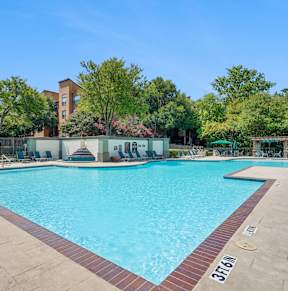 A large swimming pool surrounded by trees and a building in the background.