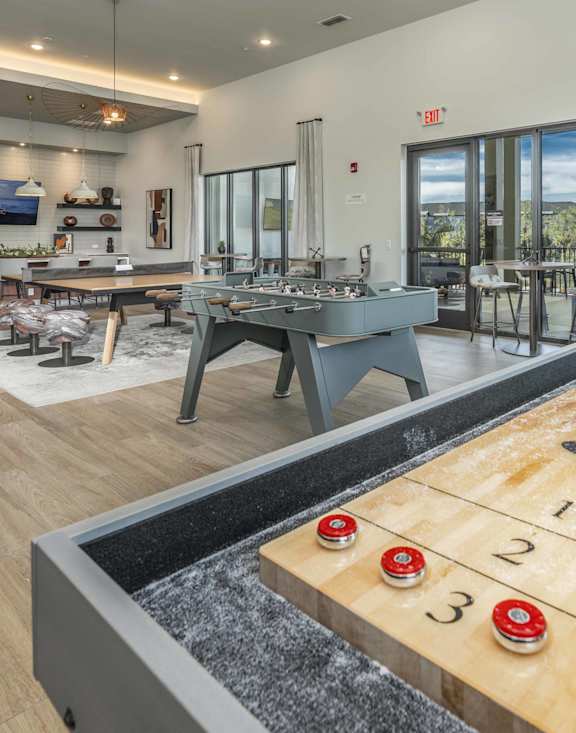 A shiny wooden air hockey table is in the middle of a room with a view of the trees outside.