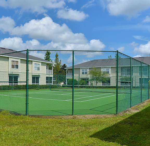 A tennis court is surrounded by a green fence and apartment buildings.