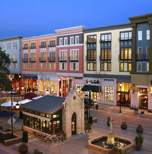 A street view of a shopping area with a fountain in the middle.