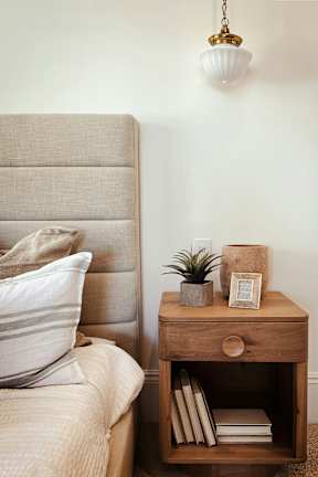 A bed with a pillow and a nightstand with a plant on it.