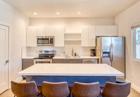 A modern kitchen with a white island and brown chairs.