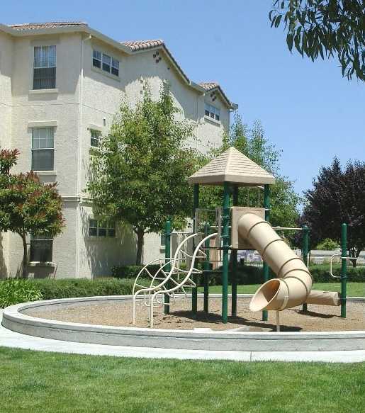 A playground with a slide and a roundabout in front of a building.