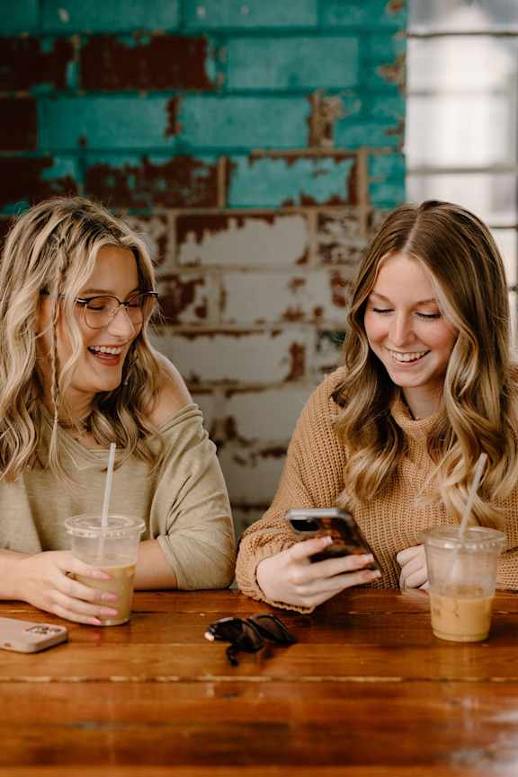 Two women sitting at a table with drinks and a smartphone.