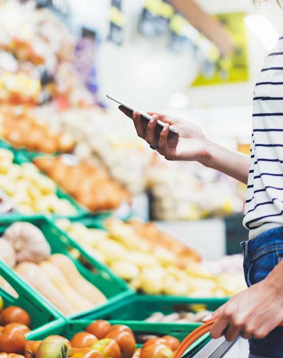 A person holding a phone and a shopping cart in a grocery store.