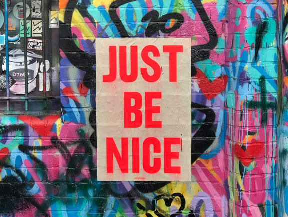 a sign that says just be nice on a wall covered in graffiti