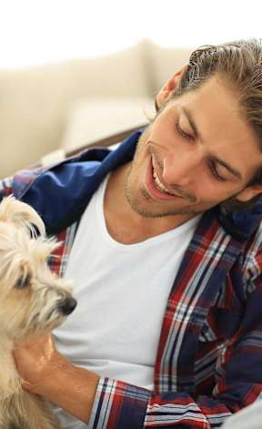 A man in a plaid shirt is holding a small dog.