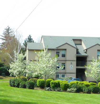 Apartment building with green lawn and trees in front.