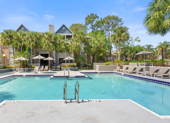 a large swimming pool with lounge chairs and umbrellas in front of a building