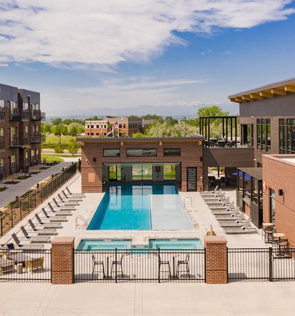 A swimming pool surrounded by a fence and chairs in front of a building.