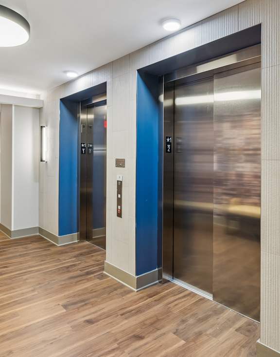 A hallway with two elevators, one blue and one silver.
