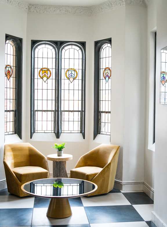 A room with a black and white checkered floor, a round table with a plant on it, and three yellow chairs.