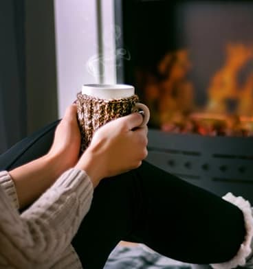Woman Holding Cup of Coffee in Front of Fireplace