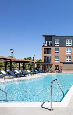 A swimming pool surrounded by sun loungers in front of apartment buildings.