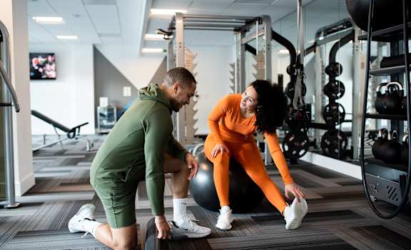 Woman on Yoga Ball and Man Stretching in Fitness Center