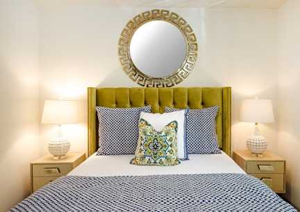 A bed with a white comforter and a green headboard with a mirror above it.