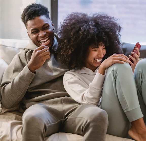 a man and woman sitting on a couch looking at a cell phone