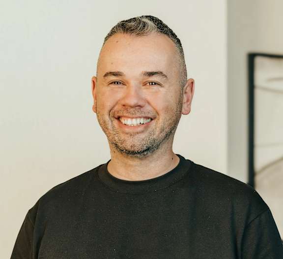 A man with a beard and short hair is wearing a black shirt and smiling.