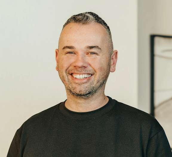 A man with a beard and short hair is wearing a black shirt and smiling.