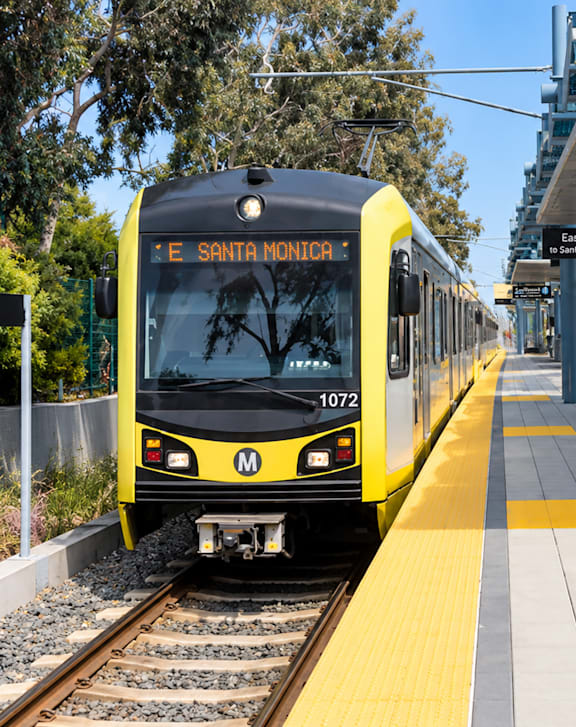 A yellow and black train with the number 1072 on it is at the E Santa Monica station.