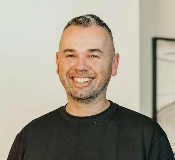 A man with a beard and short hair is wearing a black shirt and smiling.