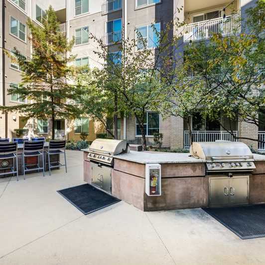 The Residences at City Center Apartments patio and grill area with grills and a table and chairs. 