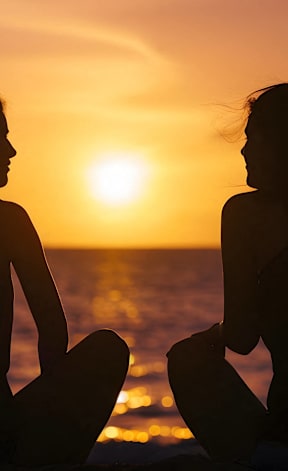 Two women sitting on the beach during sunset.
