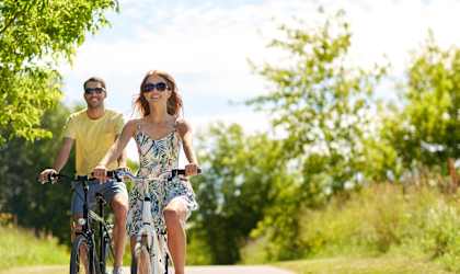 A man and a woman are riding bicycles on a paved path.
