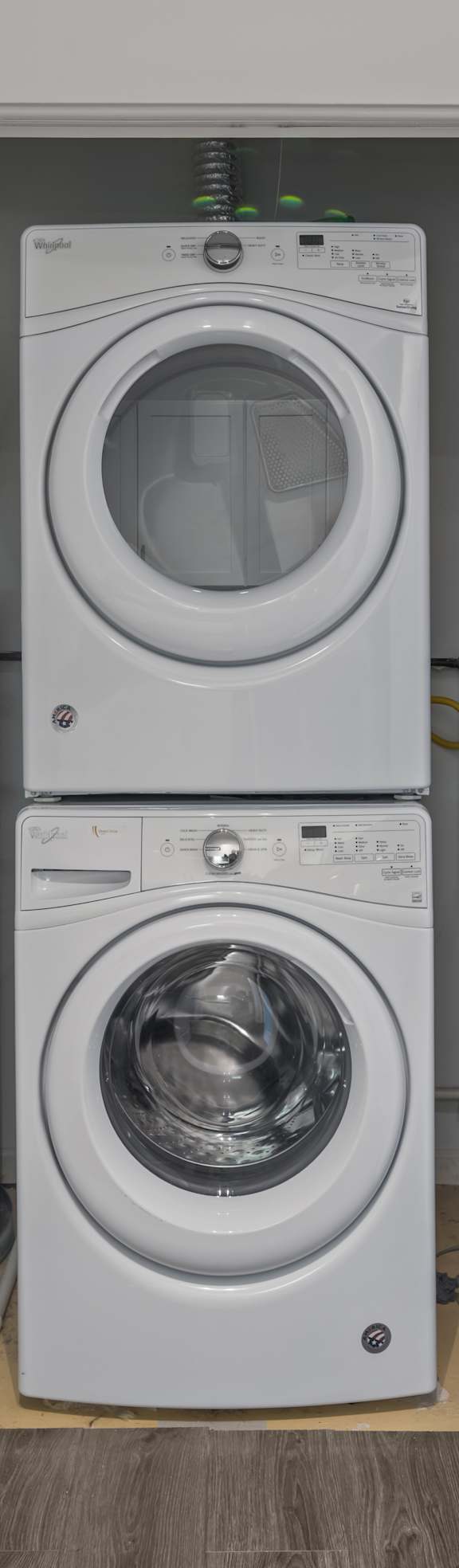 A white door is open to reveal a laundry room with a washer and dryer stacked on top of each other.