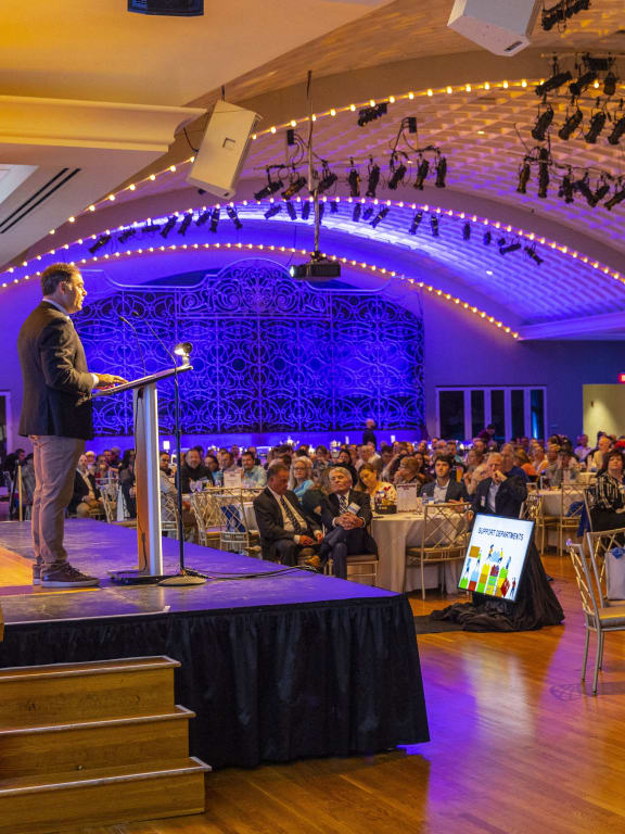 a man standing on a stage in front of a crowd of people in a room