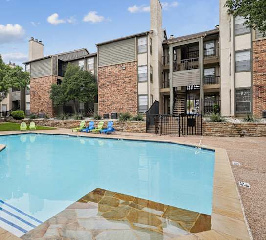 A small pool with a stone border and a few chairs around it.
