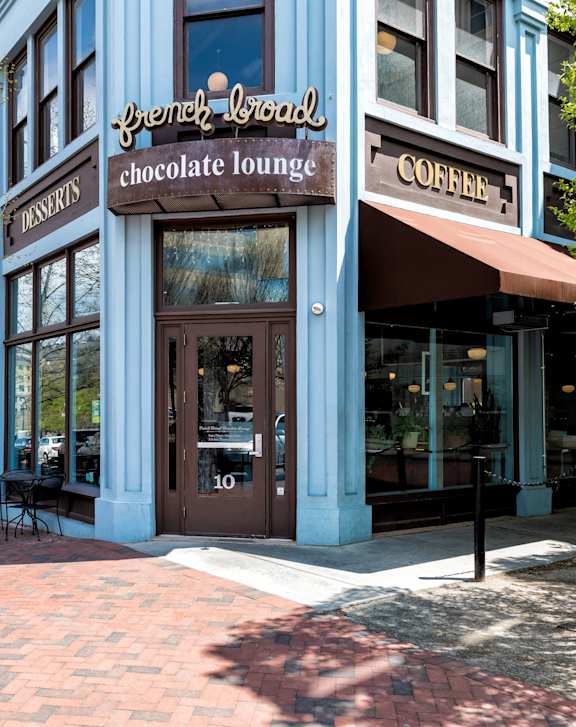 Street view of the blue French Broad Chocolate Lounge building with outdoor tables and chairs.