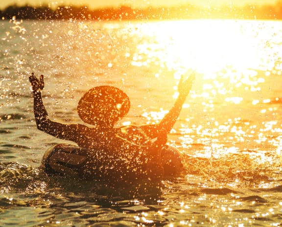 Person in Inner Tube Splashing Water While In Silhouette In Front of Sunset