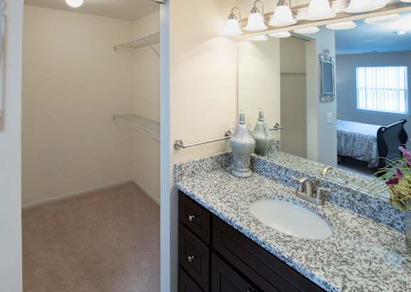 A bathroom with a sink, mirror, and a bed in the background.