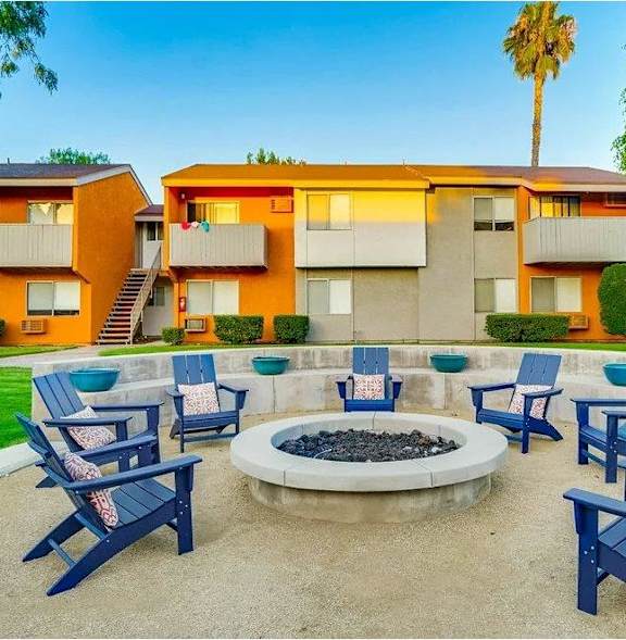 A fire pit is surrounded by blue chairs in a courtyard.