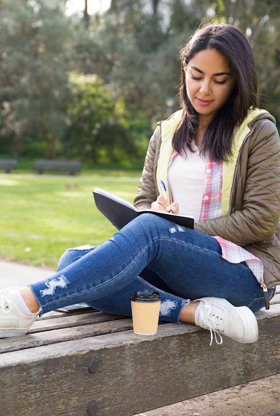 A woman is sitting on a bench writing in a notebook.