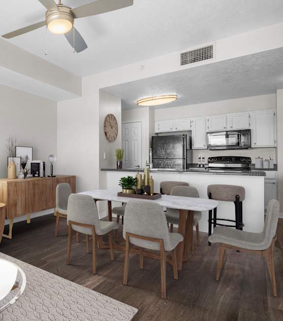 A modern living room with a grey sofa, a glass coffee table, and a kitchen area in the background.