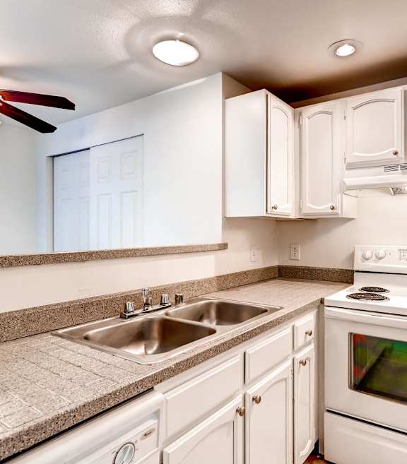 A white kitchen with a stove, sink, and cabinets.
