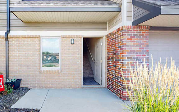 A brick apartment building with an open door to an apartment, and a patio space.