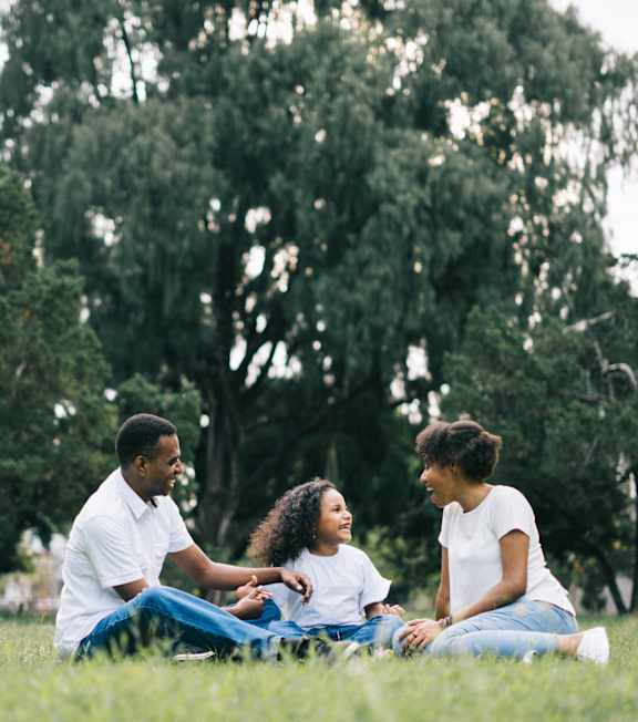 Three people sitting on the grass in a park.