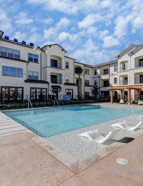 A large swimming pool in front of a building with a wooden pergola.