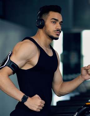A man in a black tank top is running on a treadmill.