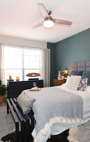 A bedroom with a bed, a chair, a ceiling fan, and a window.